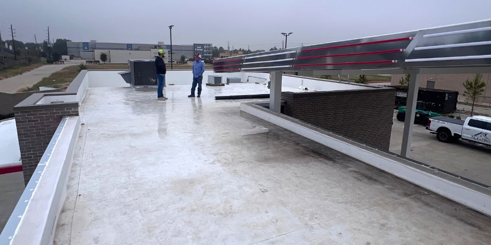 Two experienced roofing professionals inspecting a commercial TPO roofing system on a flat-roof residential structure.